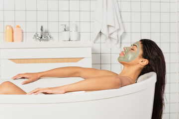 Obraz premium peaceful young african american woman with mud mask on face taking bath
