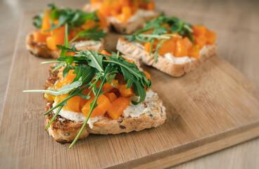 Delicious vegetarian sandwiches with pumpkin and arugula on wooden cutting board.