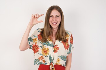 Blonde European woman over isolated background gesturing with hand showing small size, measure symbol. Smiling looking at the camera. Measuring concept.