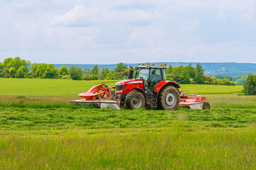 Big red tractor with two mowers mows the grass for silage