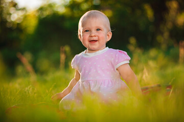 Baby girl 1 year old sitting on green grass in meadow outdoors closeup. Celebration. Childhood.