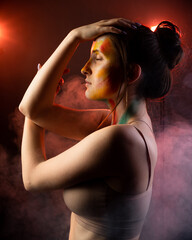 Girl with smears of paint on her face against a background of smoke illuminated by red light