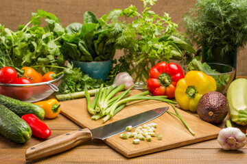 Sliced green onions and a kitchen knife on cutting board. Vegetables and greens on table.