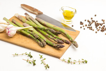 Green asparagus, garlic and a kitchen knife on a cutting board. Thyme sprigs, olive oil on table