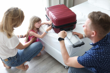 Sad little girl looks at suitcase sitting next to her parents