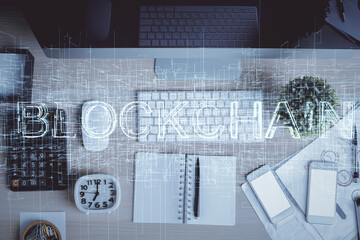 Blockchain theme hologram drawings over computer on the desktop background. Top view. Multi...