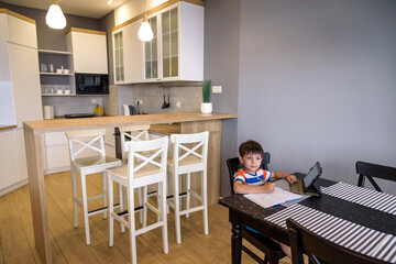 Smart preteen schoolboy doing his homework with digital tablet at home. Child using gadgets on his kitchen to study. Modern education and learning for kids