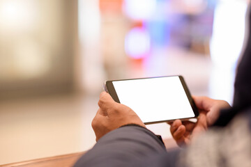 Mockup image of a man holding and using mobile phone with blank white desktop screen with on the table