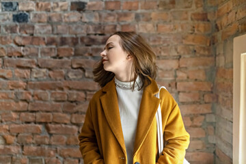 Fototapeta na wymiar Portrait of a young woman in a bright yellow coat against the background of a brick wall by the window.In the sunshine