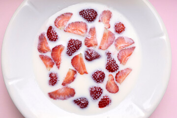 Top view of white plate full of milk and strawberries on the pink surface.Preparing ingredients for smoothie