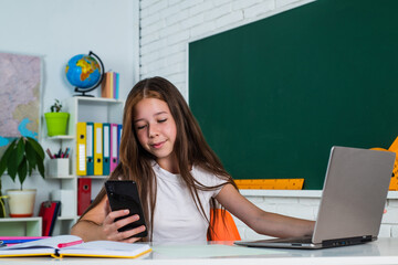 smiling teen girl making selfie on smartphone at computer in school classroom, modern life