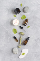 Containers of lotion, essential oils, massage rollers and gouache scraper on a gray concrete background. Natural SPA cosmetic products background. Layout of the beauty salon branding. Flat lay