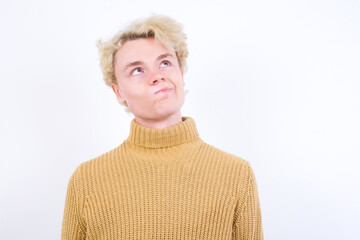 Young handsome Caucasian blond man standing against white background, looks pensively aside, plans...