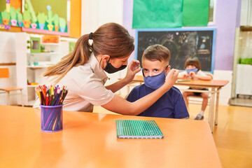 Fürsorgliche Erzieherin hilft Kind beim Maske aufsetzen