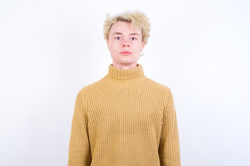 Joyful Young handsome Caucasian blond man standing against white background looking to the camera,...