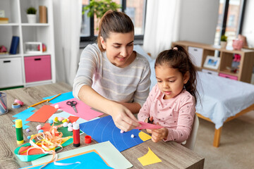 family, art and craft concept - mother spending time with her little daughter with glue making applique of color paper at home