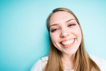 Happy girl with long hair smiling broadly looking at the camera while standing on a blue background