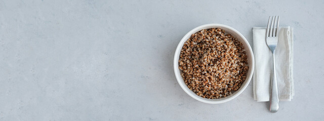 banner. Bowl of buckwheat on a grey concrete background in minimalistic style. Concept of healthy food.