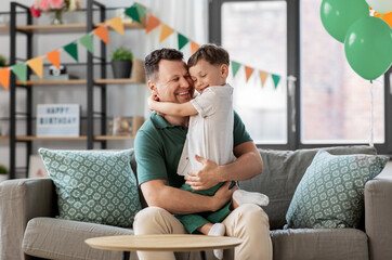 family, fatherhood and people concept - portrait of happy smiling father and little son hugging at home birthday party