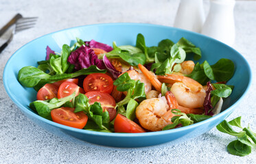 Mix salad with shrimps, tomatoes and leaves in a blue plate on the kitchen table. View from above.