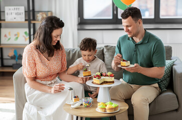 family, holidays and people concept - portrait of happy mother, father and little son eating birthday cake at home party party