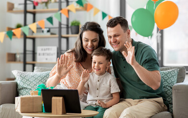 Fototapeta premium family, holidays and people concept - portrait of happy mother, father and little son with tablet pc computer and birthday gifts on table having video call at home party