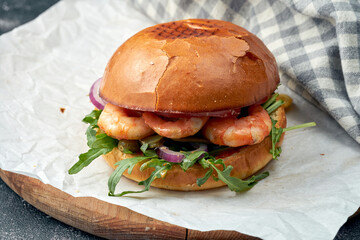 Delicious burger with prawns, arugula, onions and pickled cucumbers on white parchment. Burger with seafood. Street food