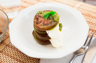 caprese salad with mozzarella, black tomatoes and pesto in white plate