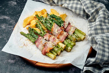 Grilled asparagus with bacon, parmesan cheese and potatoes on white parchment. Dark background