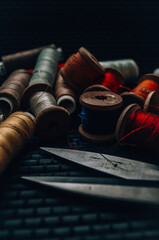 Retro sewing items: tailoring scissors, cutting knife, thimble, wooden thread spools, cushion for including pins, fabrics and sewing accessories.