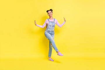 Full length photo of sweet cute young lady dressed jeans overall dancing walking isolated yellow color background