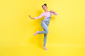 Fototapeta na wymiar Photo of carefree clubber lady stand tiptoe dance beaming white smile wear jeans overall shoes isolated yellow background