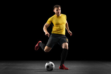 Powerful, flying above the field. Young football, soccer player in action, motion isolated on black studio background .