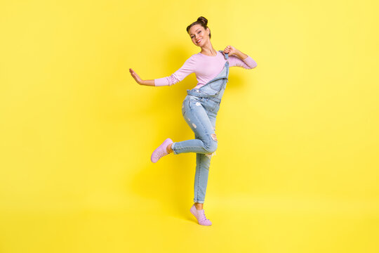 Photo of carefree clubber lady stand tiptoe dance beaming white smile wear jeans overall shoes isolated yellow background