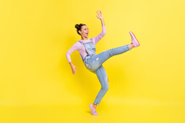 Fototapeta na wymiar Profile photo of girl stand tiptoe dance raise hand open mouth wear denim overall sneakers isolated yellow background