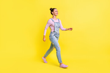 Fototapeta na wymiar Full length photo of adorable sweet young lady dressed jeans overall walking looking empty space isolated yellow color background