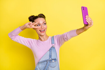 Photo of sweet funny lady dressed jeans overall recording video modern gadget v-sign cover eye isolated yellow color background