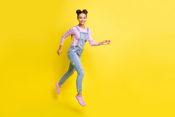 Fototapeta na wymiar Photo of cheerful lovely lady jump run beaming white smile wear jeans overall shoes isolated yellow background