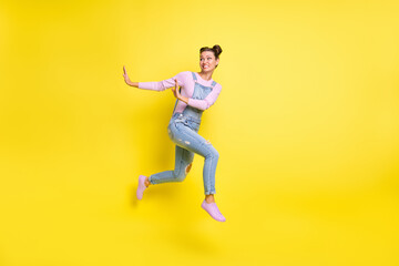 Fototapeta na wymiar Photo of scared lady jump run away show stop sign wear jeans overall sneakers isolated yellow background