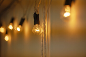 Round small bulbs with black base glowing with warm orange light hang on a white wall. Loft-style decor. The bulbs are connected to each other like a garland. Close-up