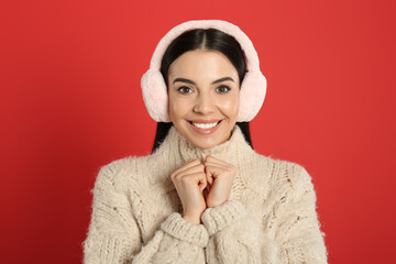 Beautiful young woman wearing earmuffs on red background