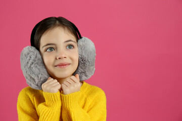 Cute little girl wearing stylish earmuffs on pink background. Space for text
