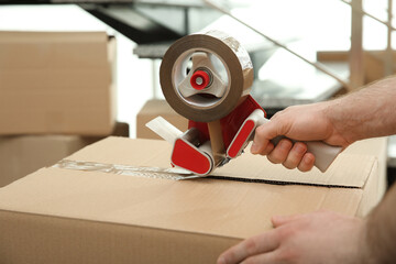 Worker taping cardboard box indoors, closeup view
