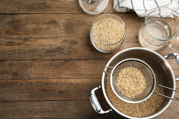 Rice and kitchenware on wooden table, flat lay. Space or text