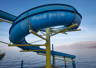 Old abandoned blue waterslide going from pier into body of water