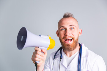 Handsome male doctor on gray background shouting in megaphone ask for attention, calling everyone for vaccine