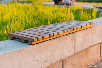 Modern wooden concrete bench in the park. Small timber. Minimalism. Wooden slats. Concrete block. Outdoor. Urban. City. Nature