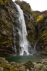 Fototapeta premium Waterfall at Ticino Valle Maggia, Maggiatal, Switzerland. At beautiful landscape scenery with colorful leaves, gras