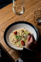 Young stylish woman is eating creamy italian risotto with basil and parmesan, top view, hands only visible