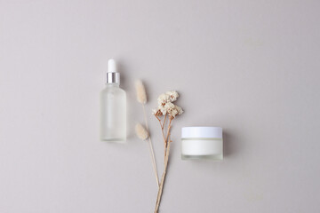 Minimal composition with cosmetic skin care products and flowers on grey background. Flat lay.